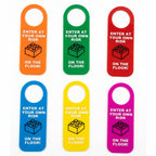 Six colorful door hangers in orange, green, red, blue, yellow, and pink, each printed with white text reading 'ENTER AT YOUR OWN RISK' and 'ON THE FLOOR!' above a black LEGO-style brick icon, arranged in two rows on a white background.