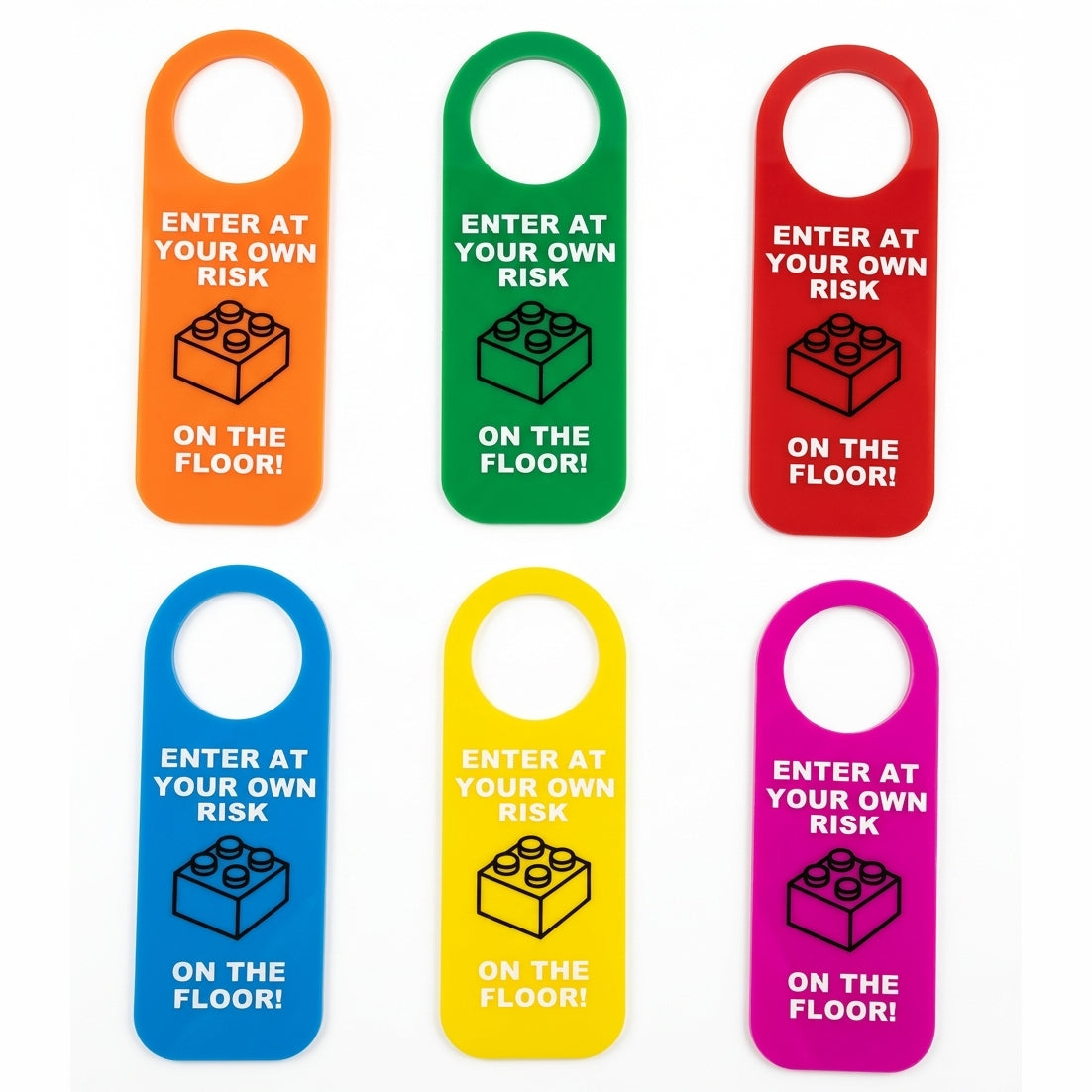Six colorful door hangers in orange, green, red, blue, yellow, and pink, each printed with white text reading 'ENTER AT YOUR OWN RISK' and 'ON THE FLOOR!' above a black LEGO-style brick icon, arranged in two rows on a white background.