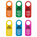 Six hanging door hangers in orange, green, red, yellow, blue, and pink, each printed with a black LEGO-style brick graphic and the text 'KEEP CALM AND BUILD ON'.