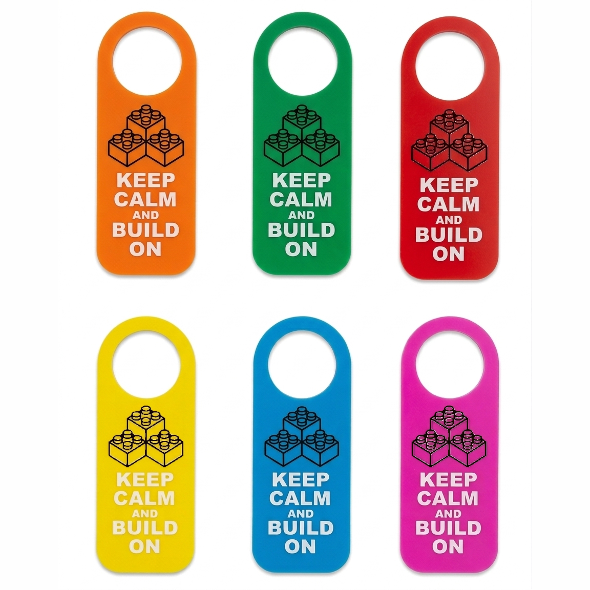 Six hanging door hangers in orange, green, red, yellow, blue, and pink, each printed with a black LEGO-style brick graphic and the text 'KEEP CALM AND BUILD ON'.
